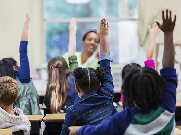 children raising their hands in a classroom, the teachers pictured being elementary education degree holders