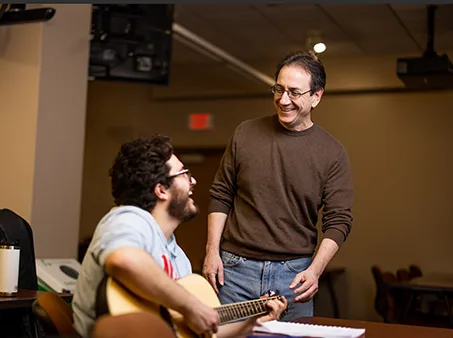 a guitar player sitting with his instructor, an example of a course at a liberal arts college