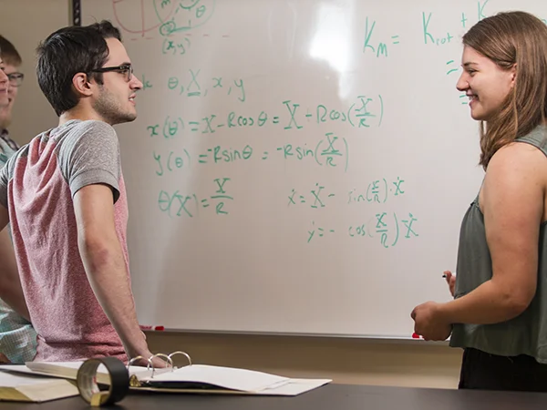 physics major students standing in front of a white board with equations on it